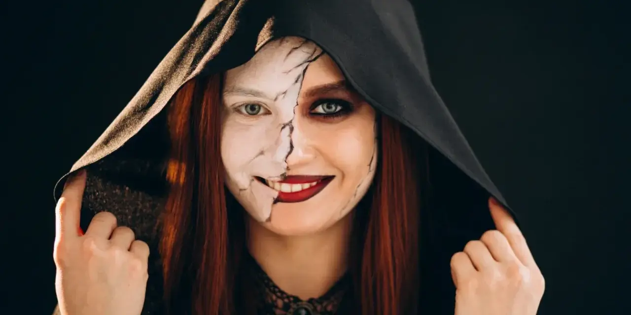 Kobieta w kapturze z połową twarzy pomalowaną na biało, z pęknięciami, druga połowa z ciemnym makijażem. Idealny prosty makijaż na Halloween.