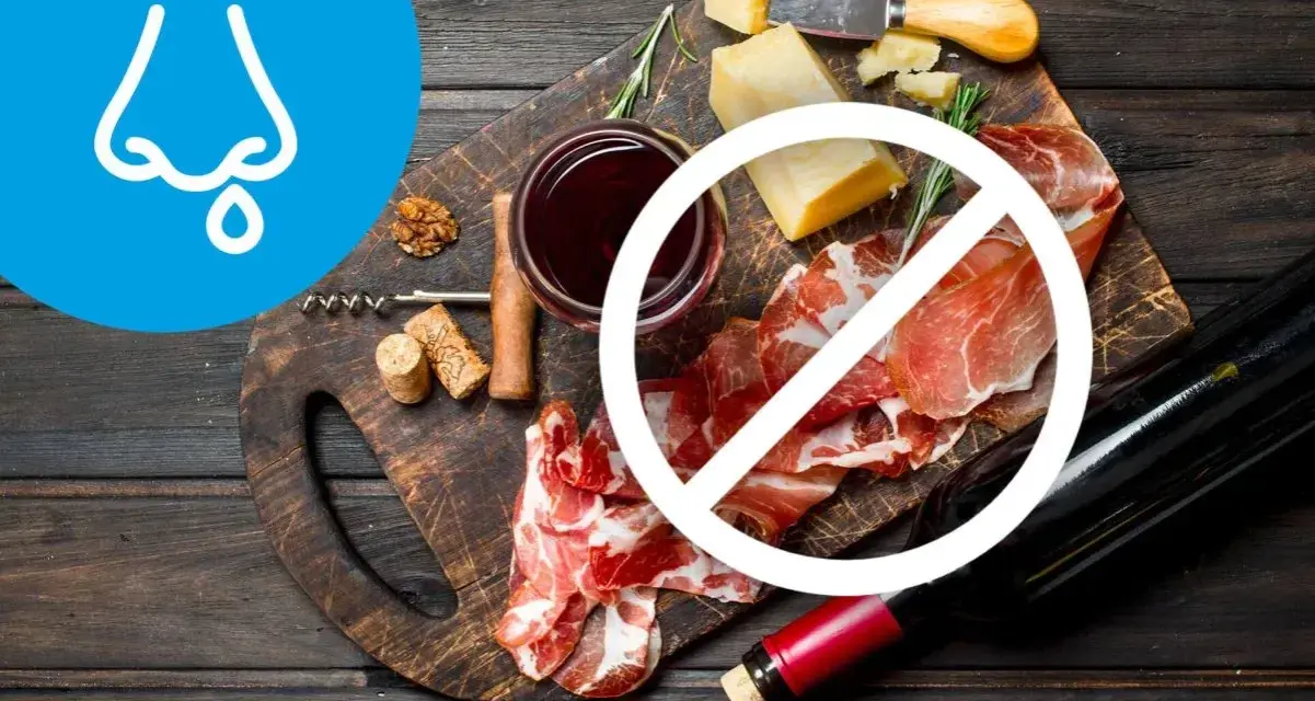 Deska serów i wędlin z winem, z symbolem zakazu. Wskazuje na dietę antyhistaminową, unikającą pewnych produktów.
