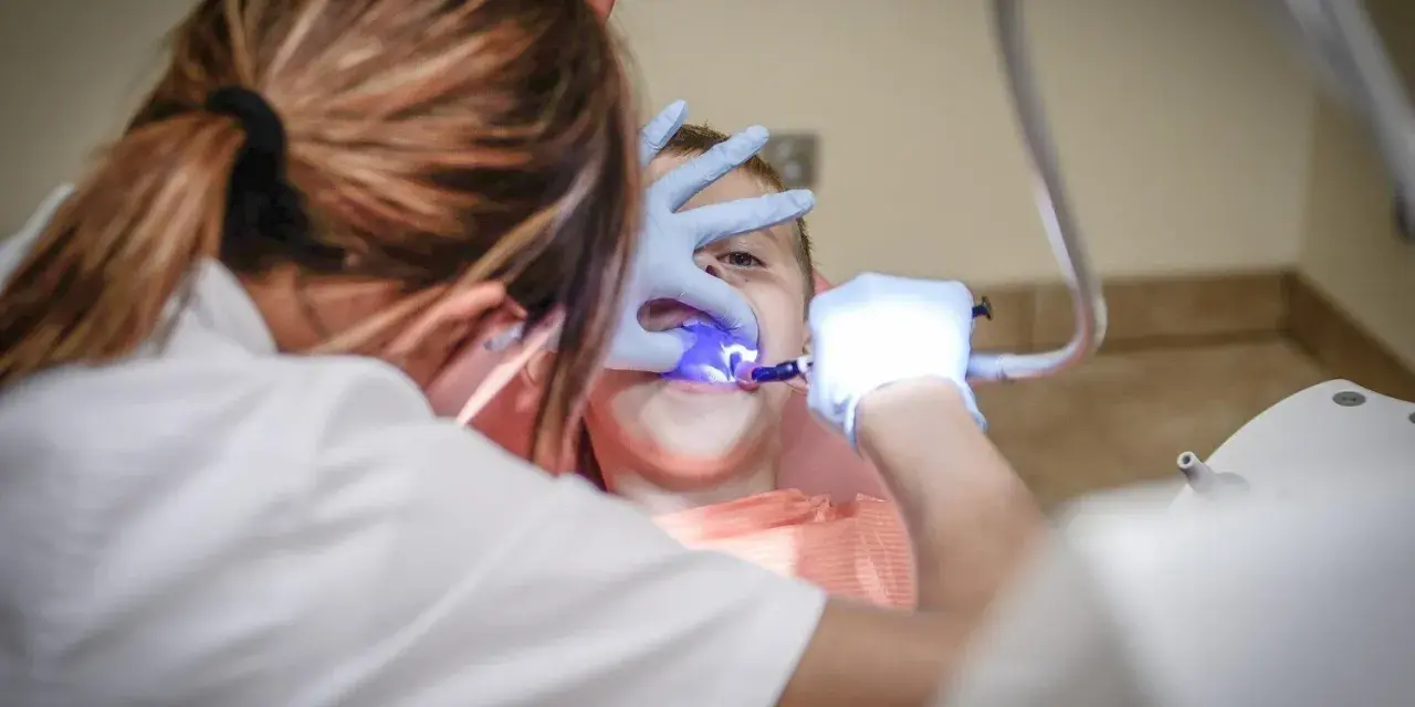 Dentysta w rękawiczkach bada zęby dziecka przy użyciu niebieskiego światła.