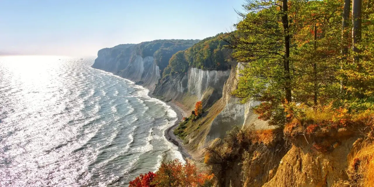 Kreidefelsen an der Ostsee, ein malerischer Anblick, der zu den beliebten Urlaubsorten zählt. Das Meer glitzert, Bäume leuchten in Herbstfarben.