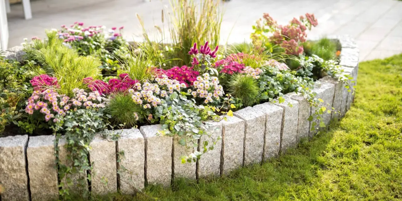 Ein wunderschön bepflanztes Beet mit bunten Blumen und Gräsern, umrandet von Granitsteinen. Perfekt, um neue Ideen für eigene Beet planen zu sammeln.