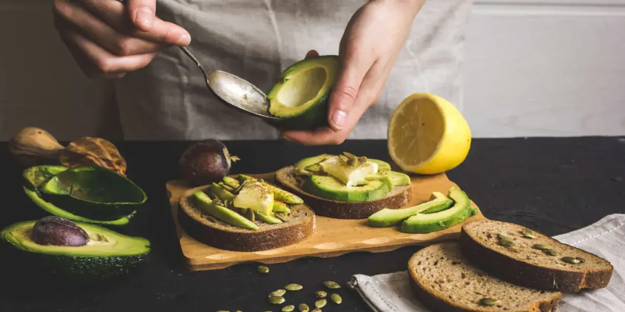 Preparazione di gustose ricette con avocado: toast con avocado, formaggio e semi.