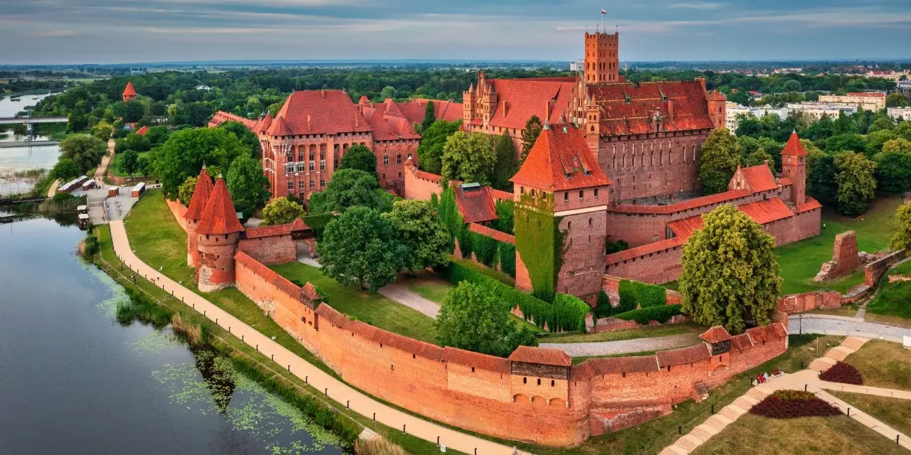 Malbork, największy zamek w Polsce, majestatycznie wznosi się nad rzeką Nogat. Czerwona cegła i strzeliste wieże tworzą imponujący widok.