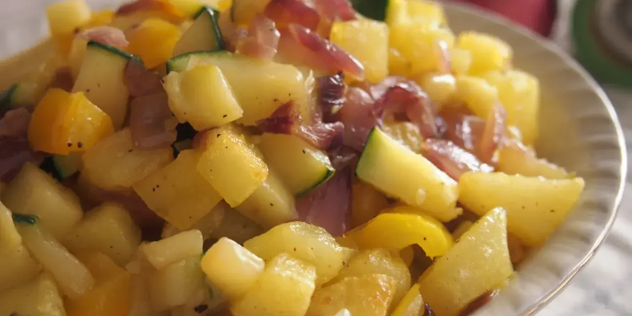 Un delicioso salteado de verduras con patatas, calabacín y pimientos amarillos, con trozos de cebolla morada.