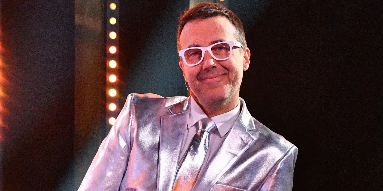 DJ Adamus w srebrnym garniturze i białych okularach, uśmiecha się. Czy to jego odpowiedź na pytanie "Jaka to melodia?