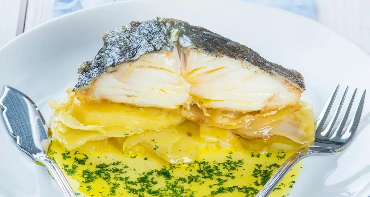 Pescado al horno con patatas y cebolla, bañado en aceite de oliva y perejil. Un plato delicioso y reconfortante.
