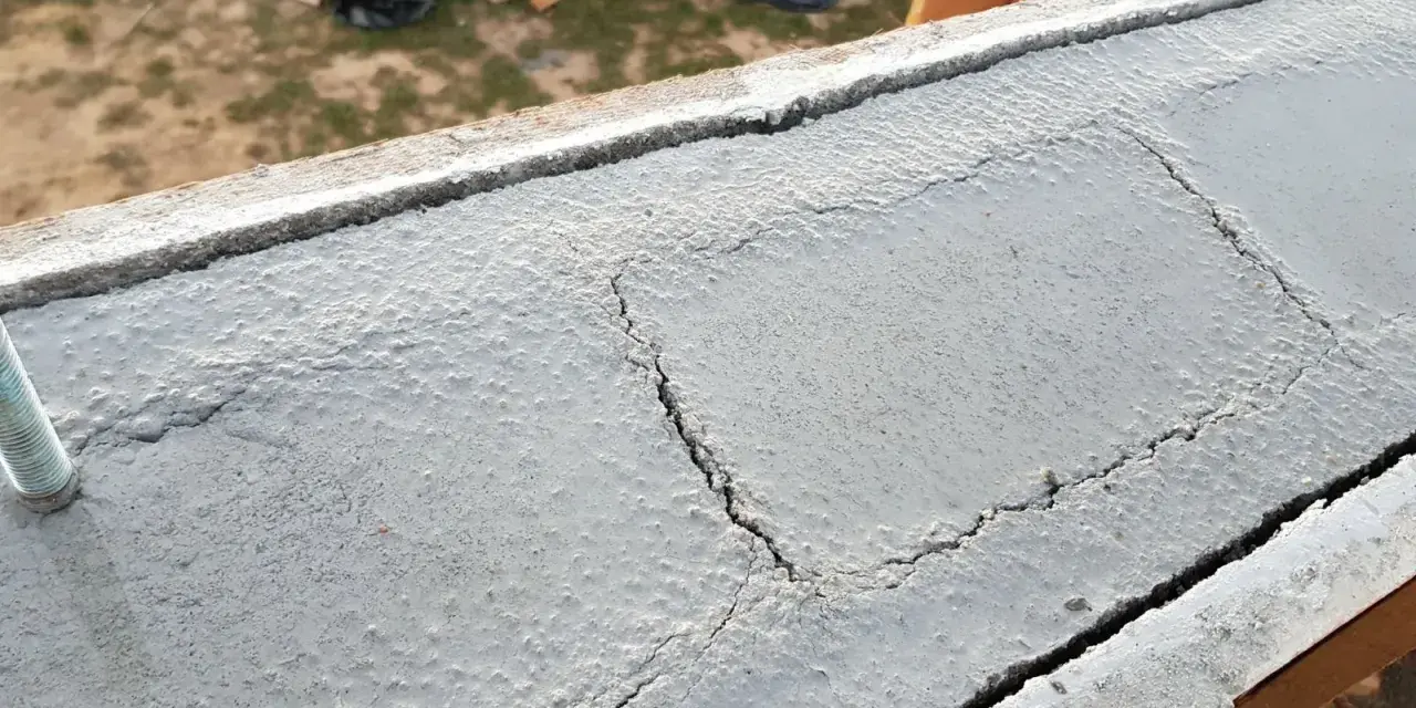 Pęknięty wieniec budowlany z widocznym prętem. Na tle plac budowy.