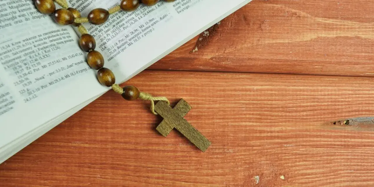 Stary różaniec na drewnianym stole obok Biblii, przypomina o 5 przykazaniach kościelnych.