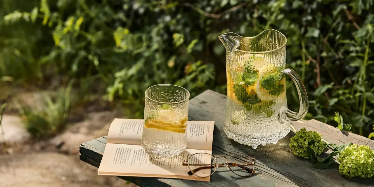 En glasburk med en alkoholfri drink, citron och mynta, står på en bok bredvid ett par glasögon.