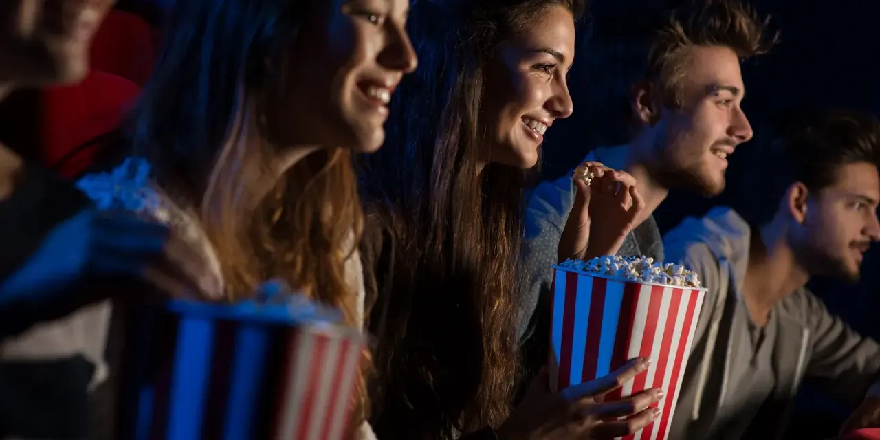 Uśmiechnięci ludzie jedzą popcorn w kinie. Idealny strój do kina to coś wygodnego, jak na przykład bluza.