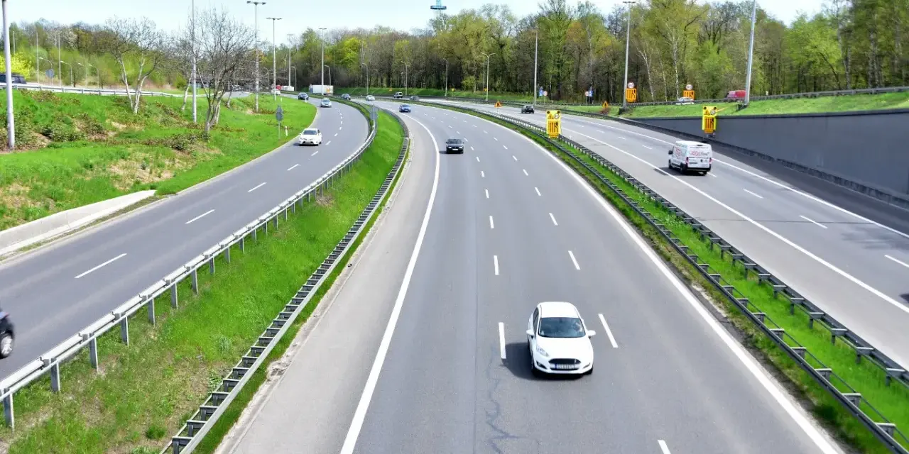 Autostrada z kilkoma samochodami i zielonymi pasami.