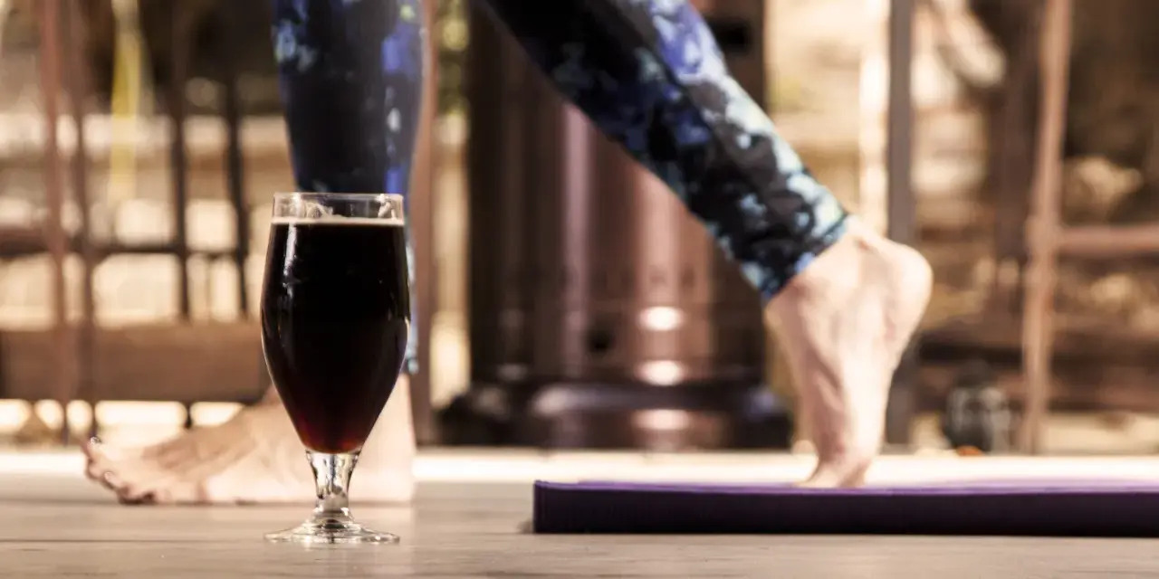 Szklanka ciemnego piwa obok maty do ćwiczeń. Czy to koniec treningu, czy nagroda? Alkohol a siłownia – dylemat.