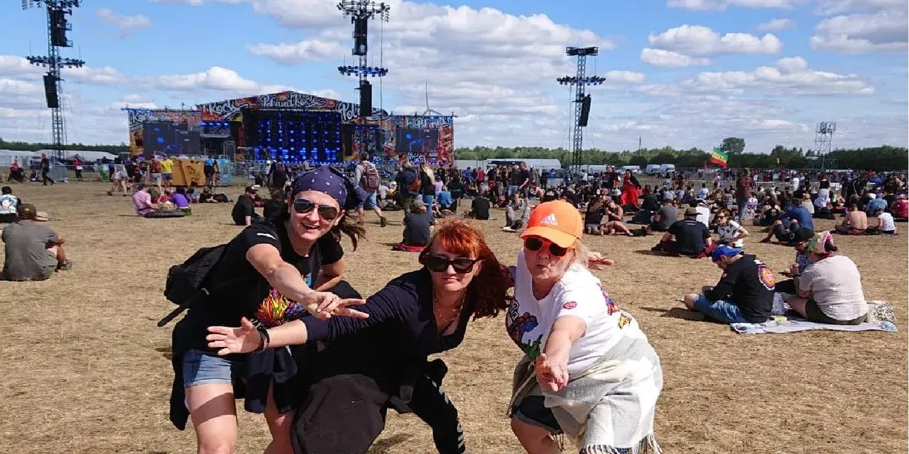 Trzy kobiety bawią się na festiwalu czaplinek pol and rock. W tle scena i tłum ludzi.