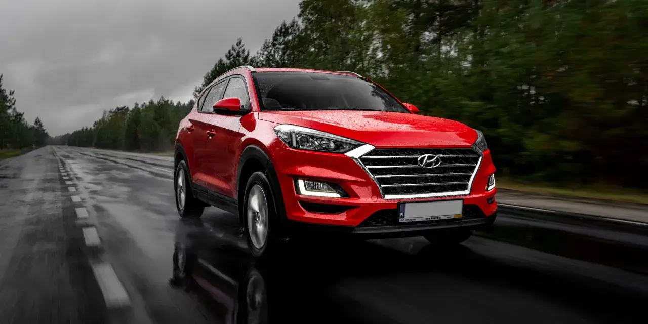 Czerwony Hyundai Tucson jedzie po mokrej drodze w deszczowy dzień. Warto pamiętać o filtrze CPL, którego zastosowanie poprawia widoczność w takich warunkach.