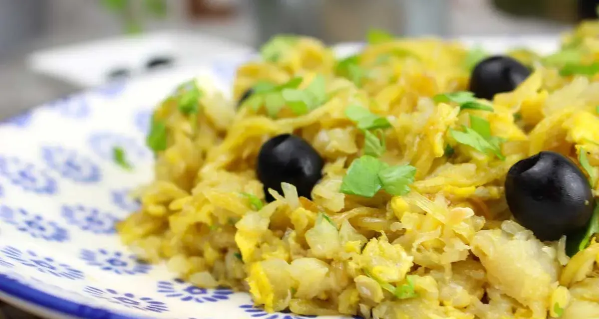Delicioso bacalao a bras, un plato tradicional con patatas finas, huevo y aceitunas negras, adornado con perejil fresco.