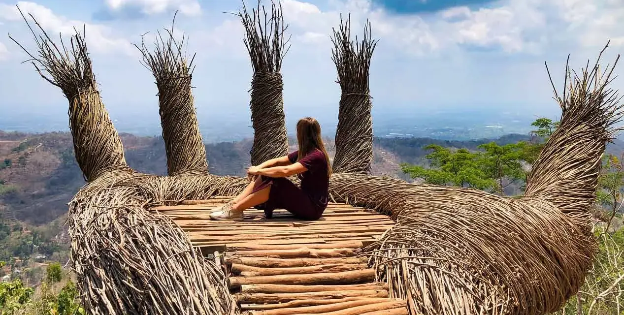 Mujer sentada en una mano gigante de ramas, disfrutando de la vista. Un lugar perfecto para viajar a Java, Indonesia.
