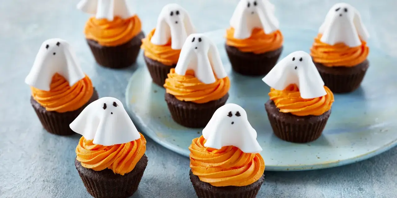 Sju chokladmuffins med orange frosting och vita spökdekorationer. Perfekt att baka till Halloween med barnen!