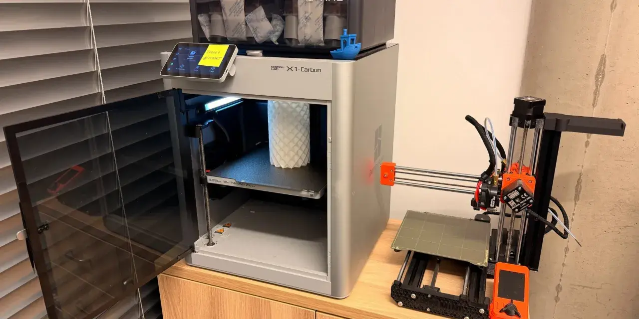 Test drukarki 3D Bambu Lab X1-Carbon z AMS i małą drukarką Prusa Mini obok.