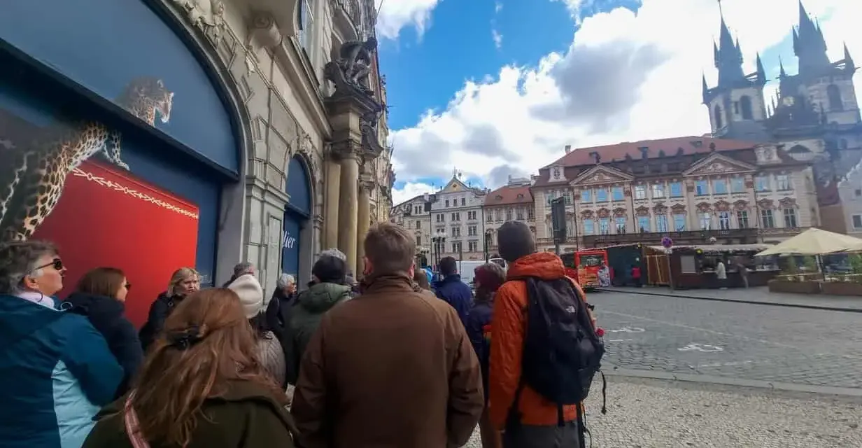 A group of tourists on a prague free walking tour gather on a cobblestone street, with historic buildings and a church in the background.