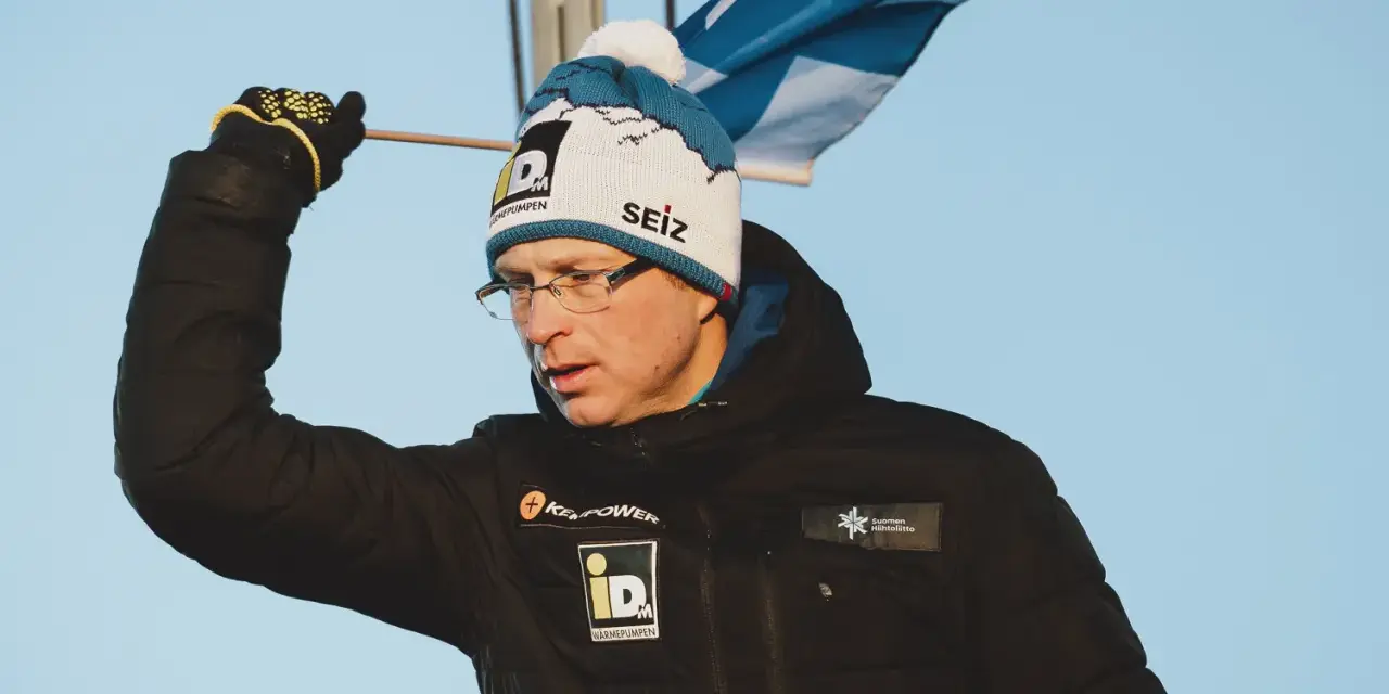 Igor Medved w czapce z pomponem i flagą Finlandii, w czarnej kurtce z logo.