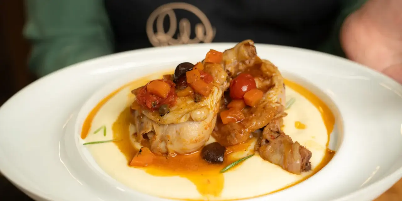Pollo alla cacciatora succulento su un letto di polenta cremosa, guarnito con pomodorini, olive e carote.