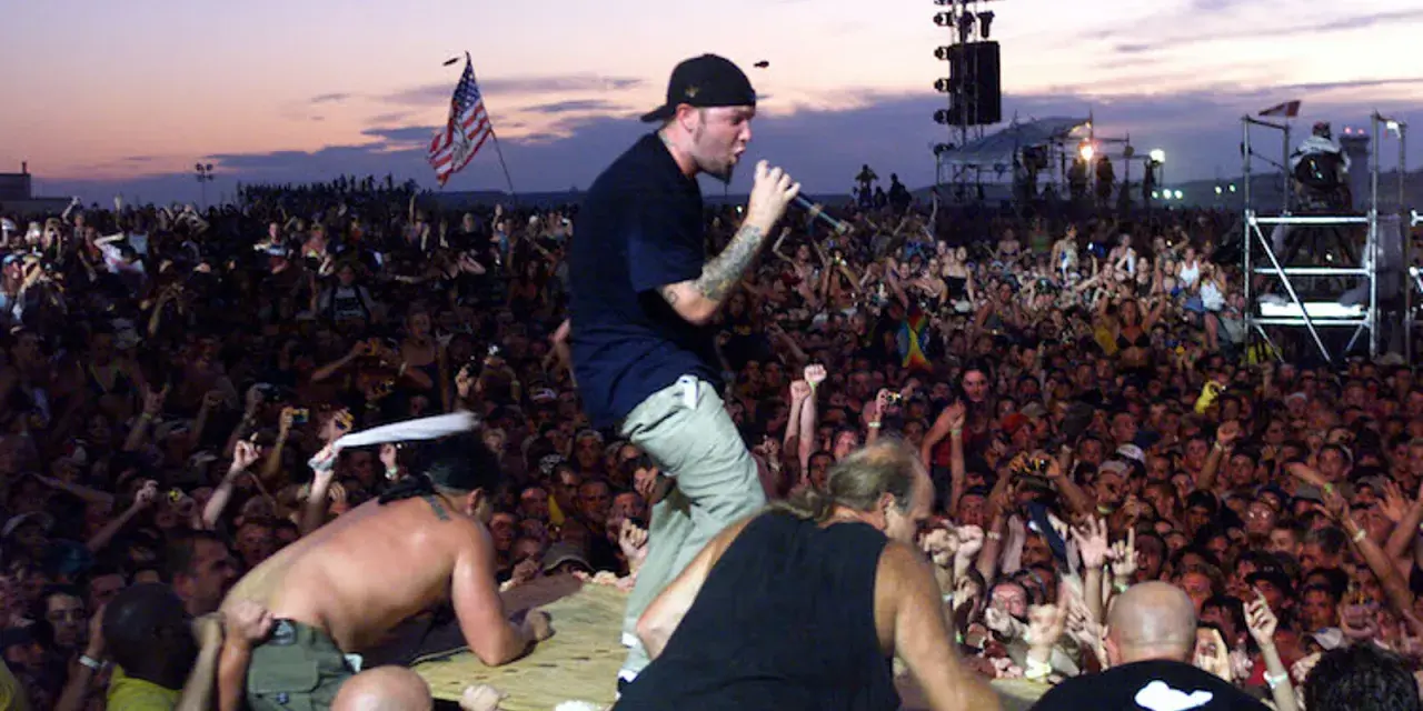 Tłum na Woodstock 99, z wokalistą na scenie i amerykańską flagą. Atmosfera była napięta, co doprowadziło do późniejszych zamieszek i ofiar.
