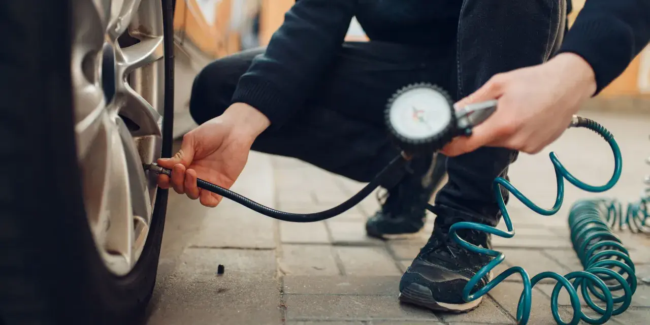 Persona controlla la pressione degli pneumatici dell'auto con un manometro, seguendo la tabella pressione pneumatici auto per la sicurezza.