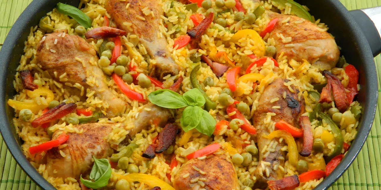 Pyszna paella z kurczakiem, ryżem, papryką i groszkiem w dużej patelni.
