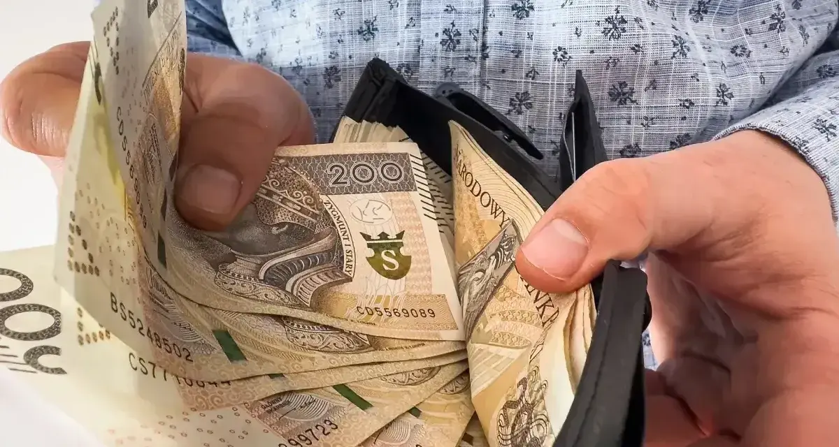 Dłonie trzymają portfel z banknotami 200 zł. Ile trzeba przepracować, by zasłużyć na taką 13 pensję?