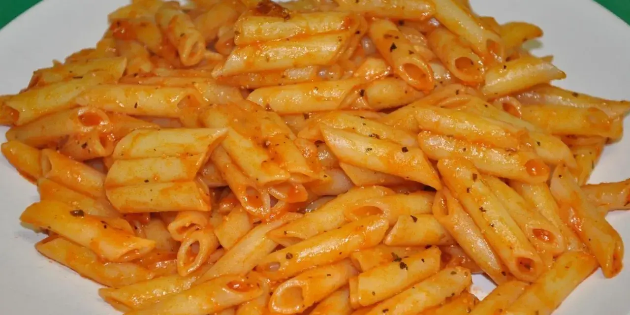 Macarrones penne con salsa de tomate y hierbas en un plato blanco.