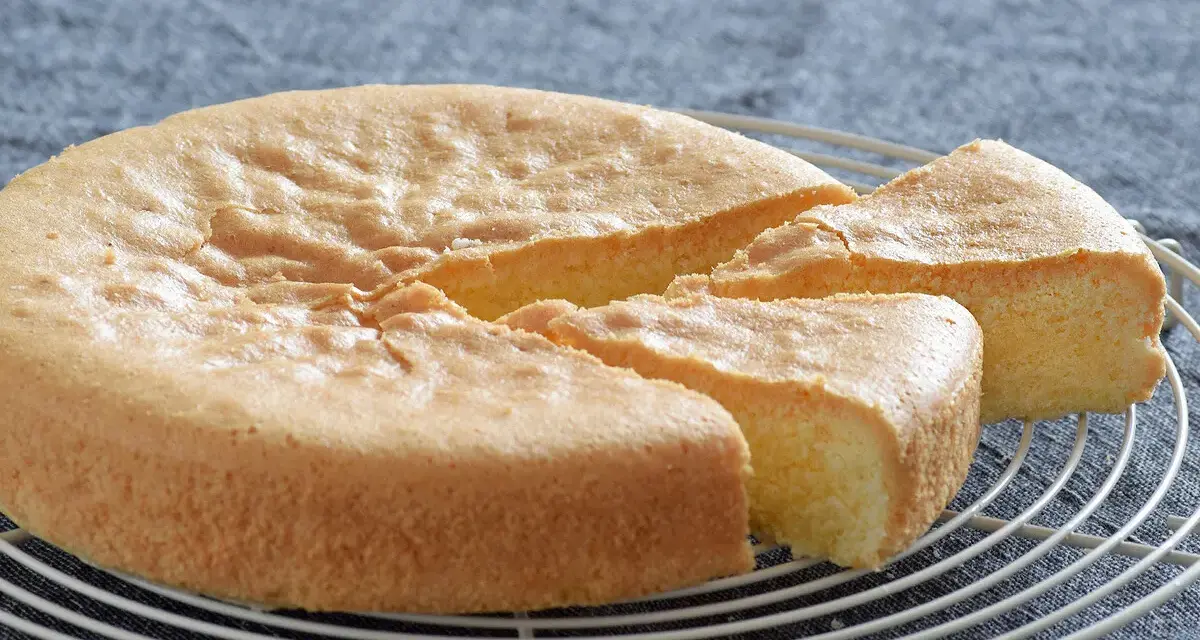 Bizcocho sin gluten esponjoso y dorado, recién cortado en porciones sobre una rejilla.
