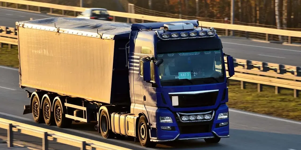 Niebieska ciężarówka z naczepą jedzie autostradą. Kierowca posiada świadectwo kwalifikacji zawodowej, co pozwala mu na bezpieczne przewożenie towarów.