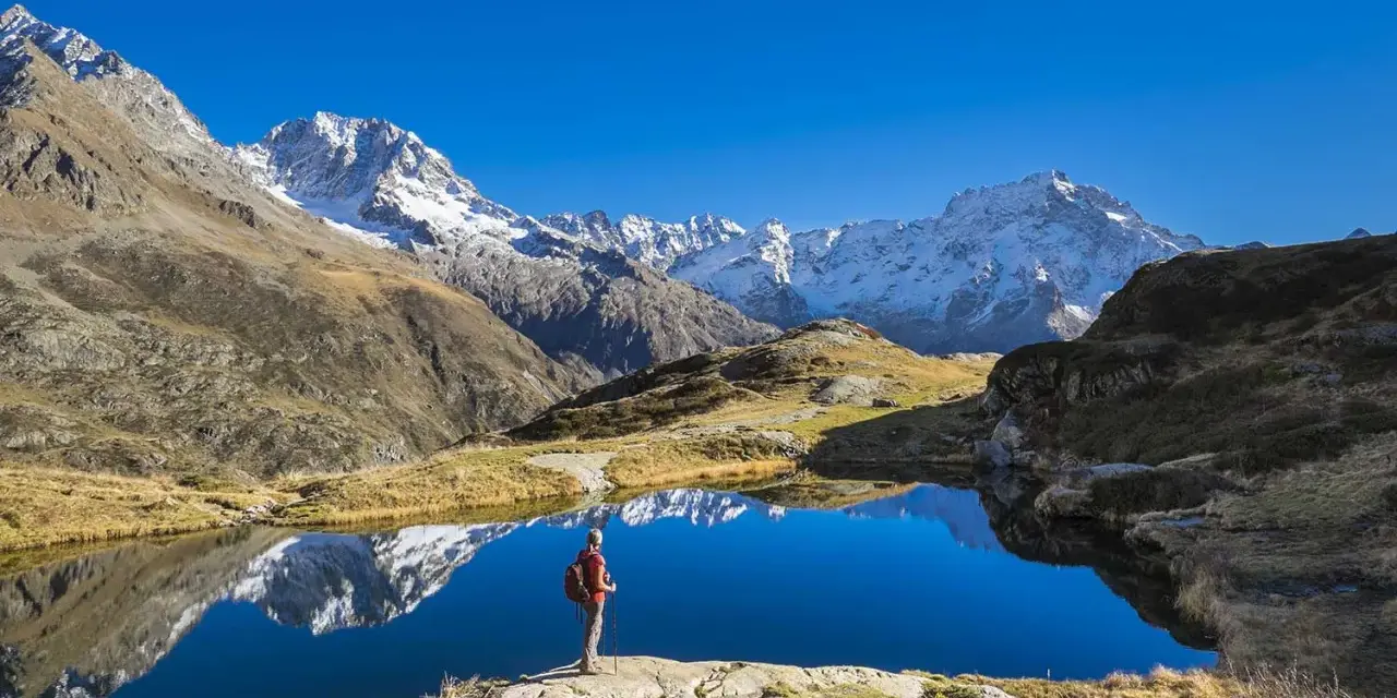 Randonneur contemplant un lac alpin aux reflets parfaits, un paysage grandiose qui pourrait faire partie d'un GR5 itinéraire complet.