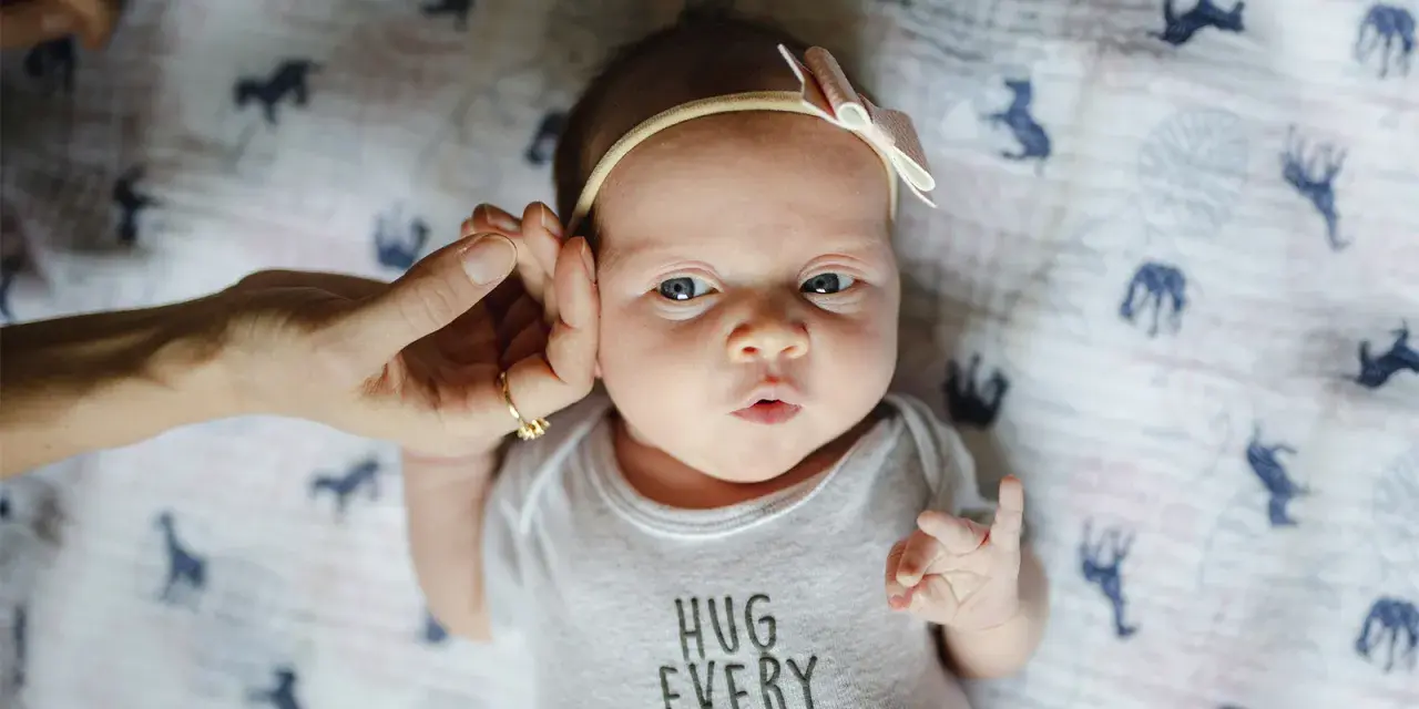 Uroczy 3 tygodniowy noworodek w body z napisem "HUG EVERY DAY", z delikatną opaską na głowie.