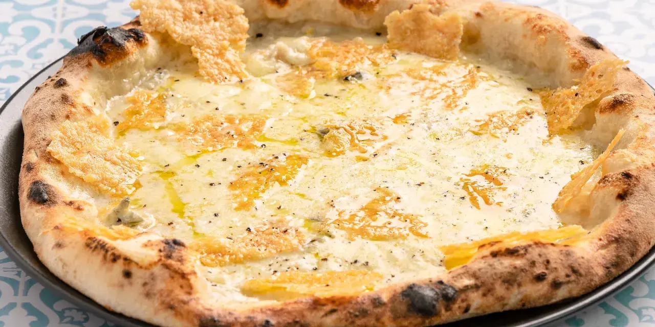 Eine köstliche Pizza quattro formaggi mit geschmolzenem Käse und knusprigem Rand auf einem gemusterten Tisch.