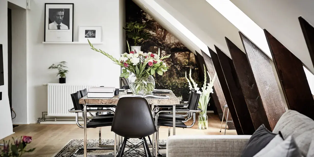 Välkomnande inredd vindsvåning med snedtak, matplats med blommor och konst.
