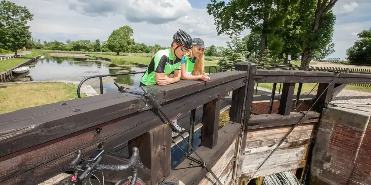 Para rowerzystów odpoczywa przy śluzie, podziwiając malownicze **trasy rowerowe Augustów**.