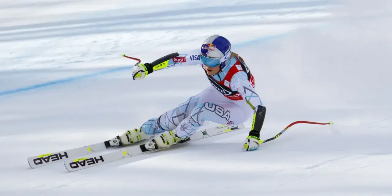 Lindsey Vonn w pełnym pędzie, w białym kombinezonie z napisem USA, na nartach HEAD. Widoczny moment tuż przed upadkiem.