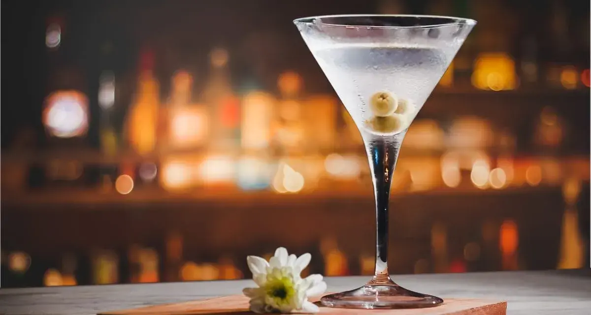 Elegancki kieliszek z orzeźwiającym martini extra dry, ozdobiony oliwkami, stoi na blacie. W tle rozmyte światła baru.