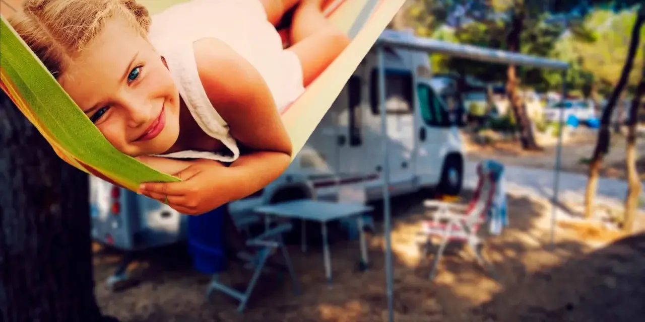 Ein glückliches Mädchen entspannt sich in einer Hängematte auf einem familienfreundlichen Campingplatz. Im Hintergrund stehen Wohnmobile und Campingmöbel.