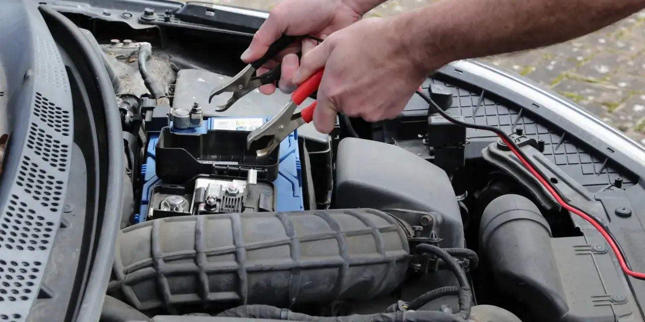 Ręce podłączają kable do akumulatora, bo auto nie odpala.