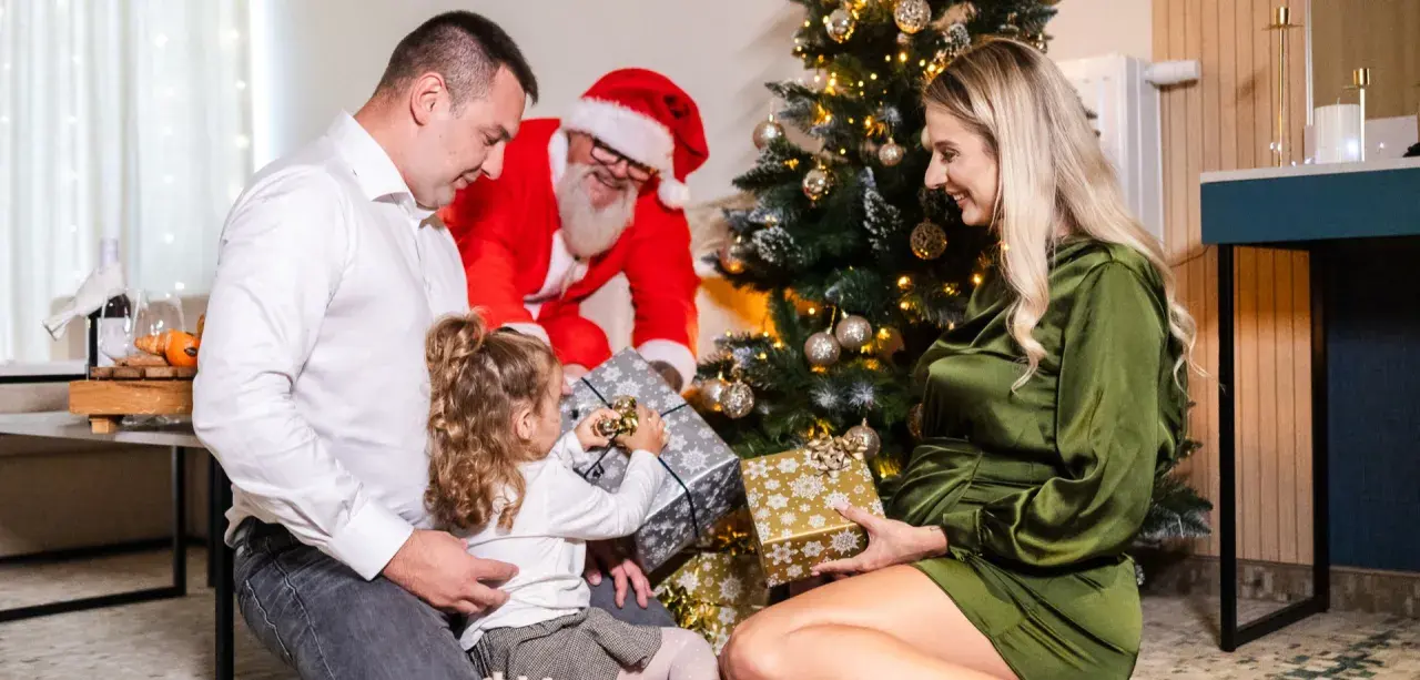 Rodzina otwiera prezenty przy choince, a Mikołaj uśmiecha się w tle. Wesołe święta w hotelu.