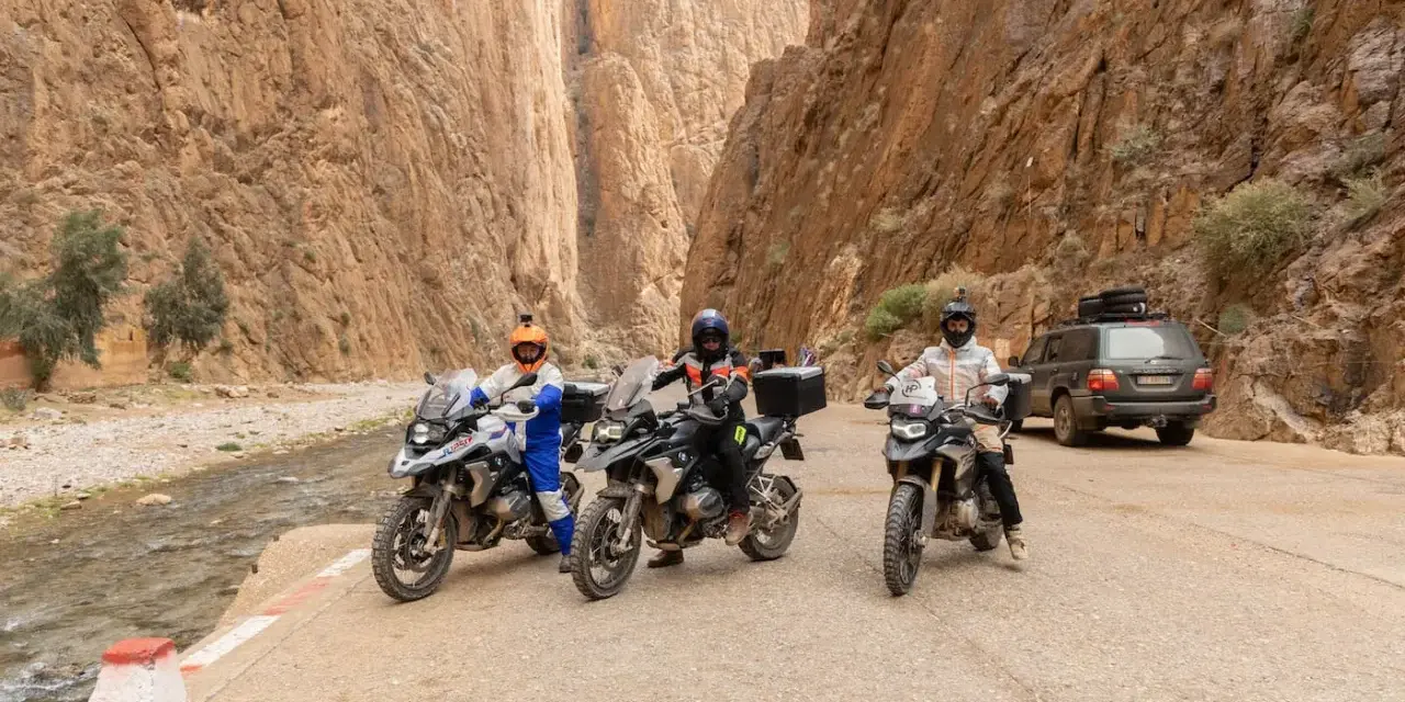 Tre moto e un fuoristrada pronti per avventurosi itinerari in moto in Marocco, tra canyon mozzafiato e un fiume.