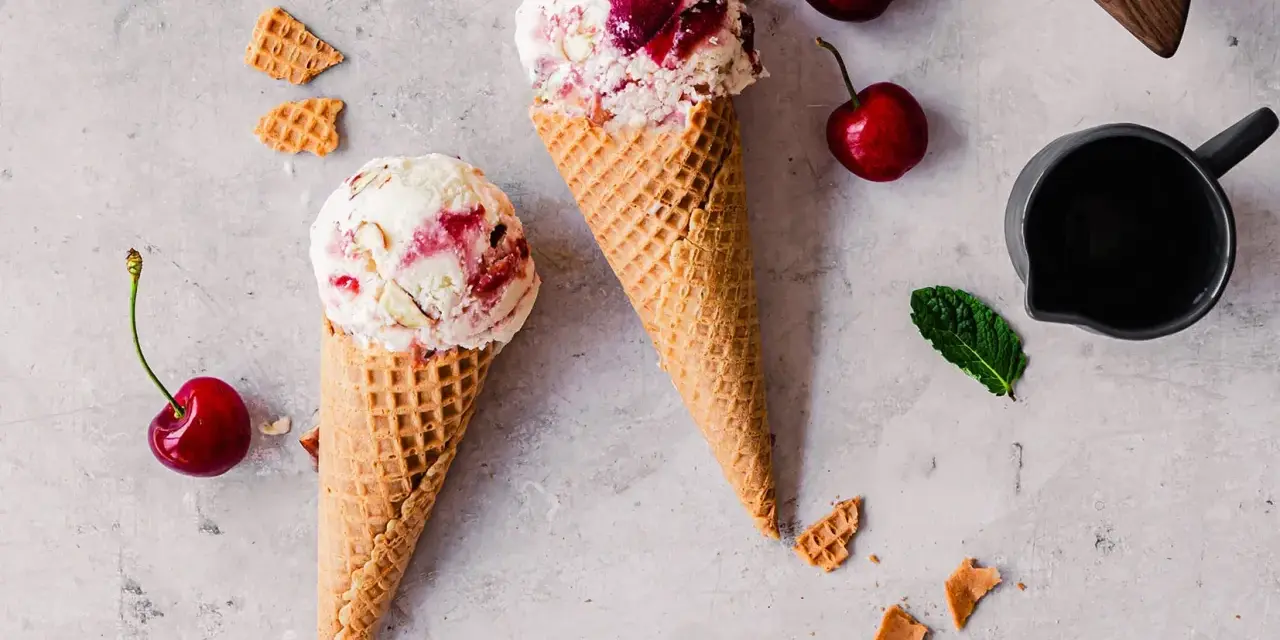 Zwei Waffelhörnchen mit Joghurt Kirsch Eis, garniert mit frischen Kirschen und Minze.