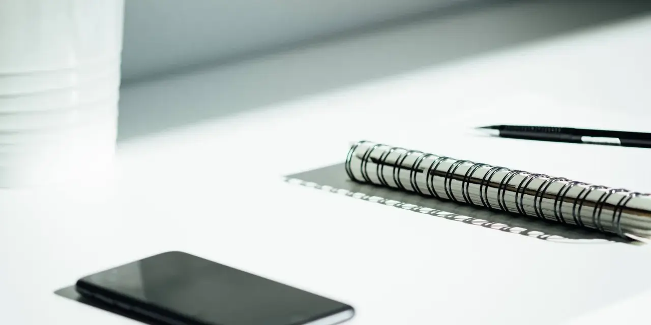 A smartphone, notebook, and pen sit on a desk, ready for a startup auditor's analysis.