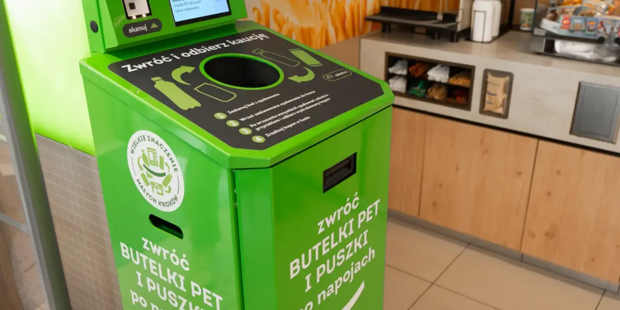 Zielony automat do zwrotu butelek PET i puszek. Skanuj kod, wrzuć opakowanie, by zdjąć zabezpieczenie sklepowe z butelki i otrzymać kaucy.