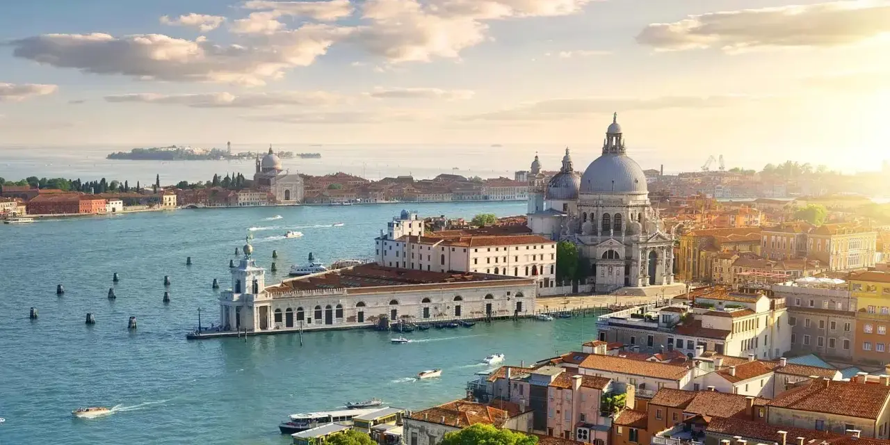 Venice cityscape with canals, boats, and historic buildings under a sunny sky.