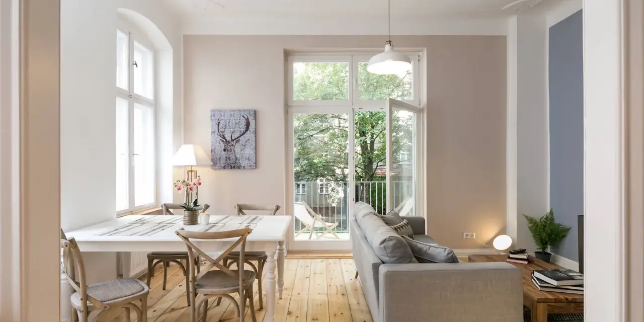 Gemütliches 15 qm Wohnzimmer mit Essbereich einrichten: heller Esstisch, graue Stühle, Sofa, Holzboden, Fenster mit Blick ins Grüne.