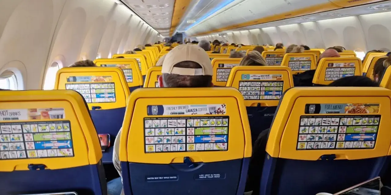 Widok wnętrza samolotu Ryanair z żółtymi oparciami siedzeń i instrukcjami bezpieczeństwa.