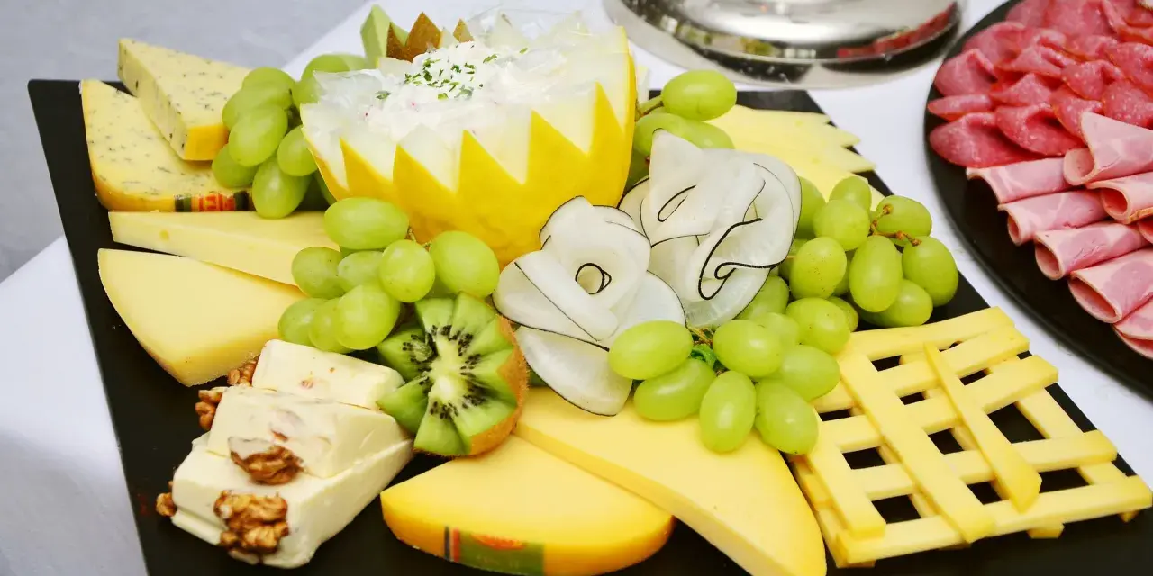 Plateau de fromage festif avec raisins verts, kiwi, noix et charcuterie. Une belle décoration plateau de fromage pour un événement.